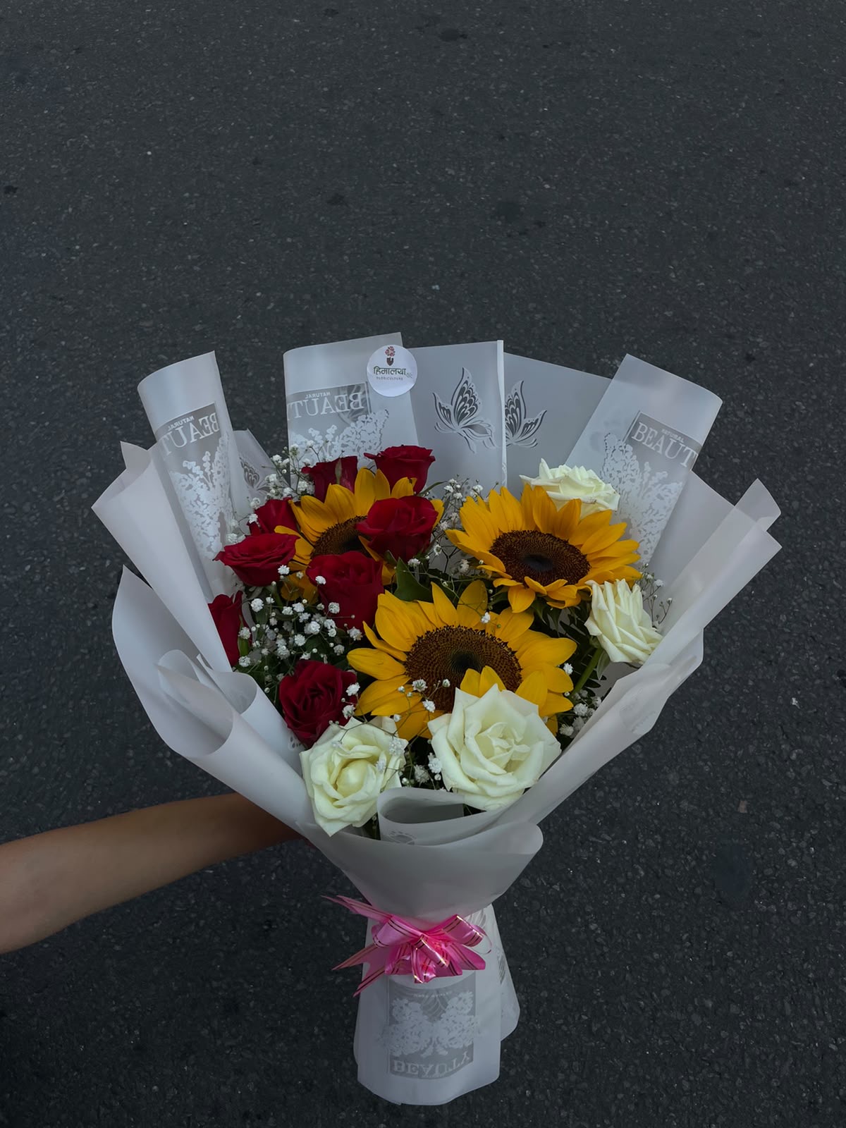 A fresh mix of bright sunflowers with red and white roses, beautifully wrapped in white with a soft pink ribbon.