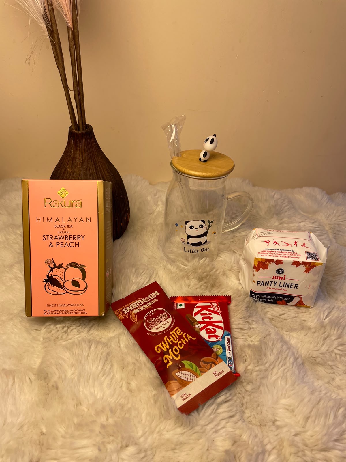 Cozy Snack Hamper A practical and cheerful combination featuring flavored black tea, a glass tumbler, panty liner, protein bar, and KitKat.