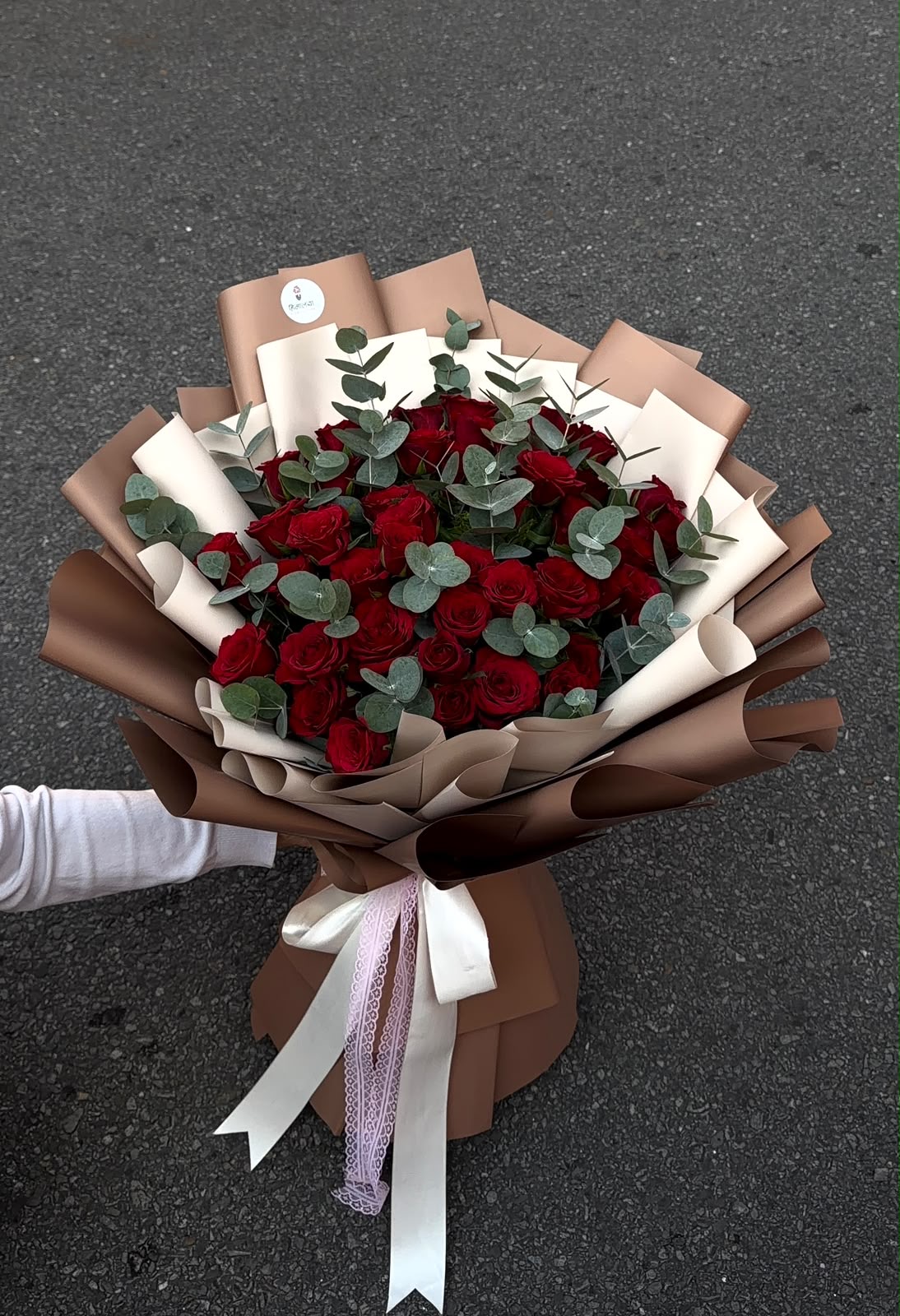 A grand and romantic arrangement featuring 50 red roses, beautifully complemented by Dollar foliage and finished with premium white and brown wrapping. White and baby pink ribbons add an elegant finishing touch.