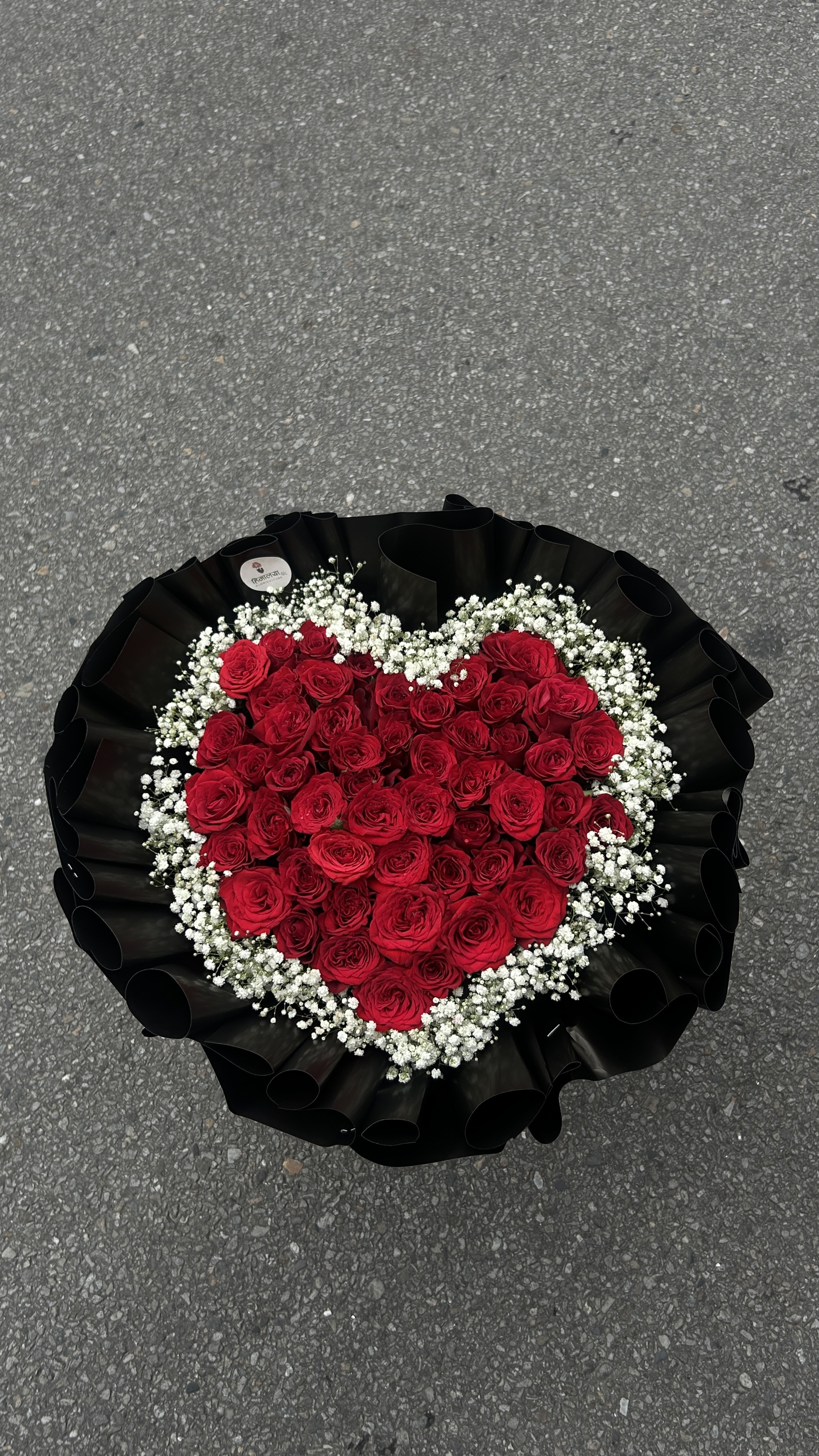 A grand and romantic floral arrangement featuring 50 stems of fresh red roses, beautifully complemented with delicate Gypsophila (Gipsy). The bouquet is creatively wrapped in heart-shaped black paper, creating a bold and luxurious presentation.