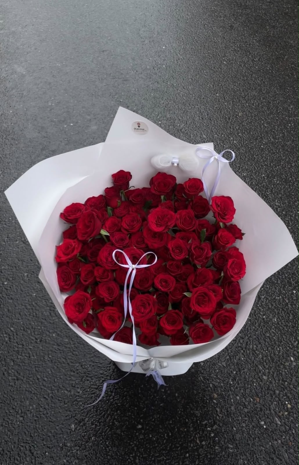 A grand and elegant floral arrangement featuring 100 stems of fresh red roses, beautifully arranged on an Oasis base and finished with a premium white wrapper and white ribbon. The full design creates a luxurious and impressive presentation.