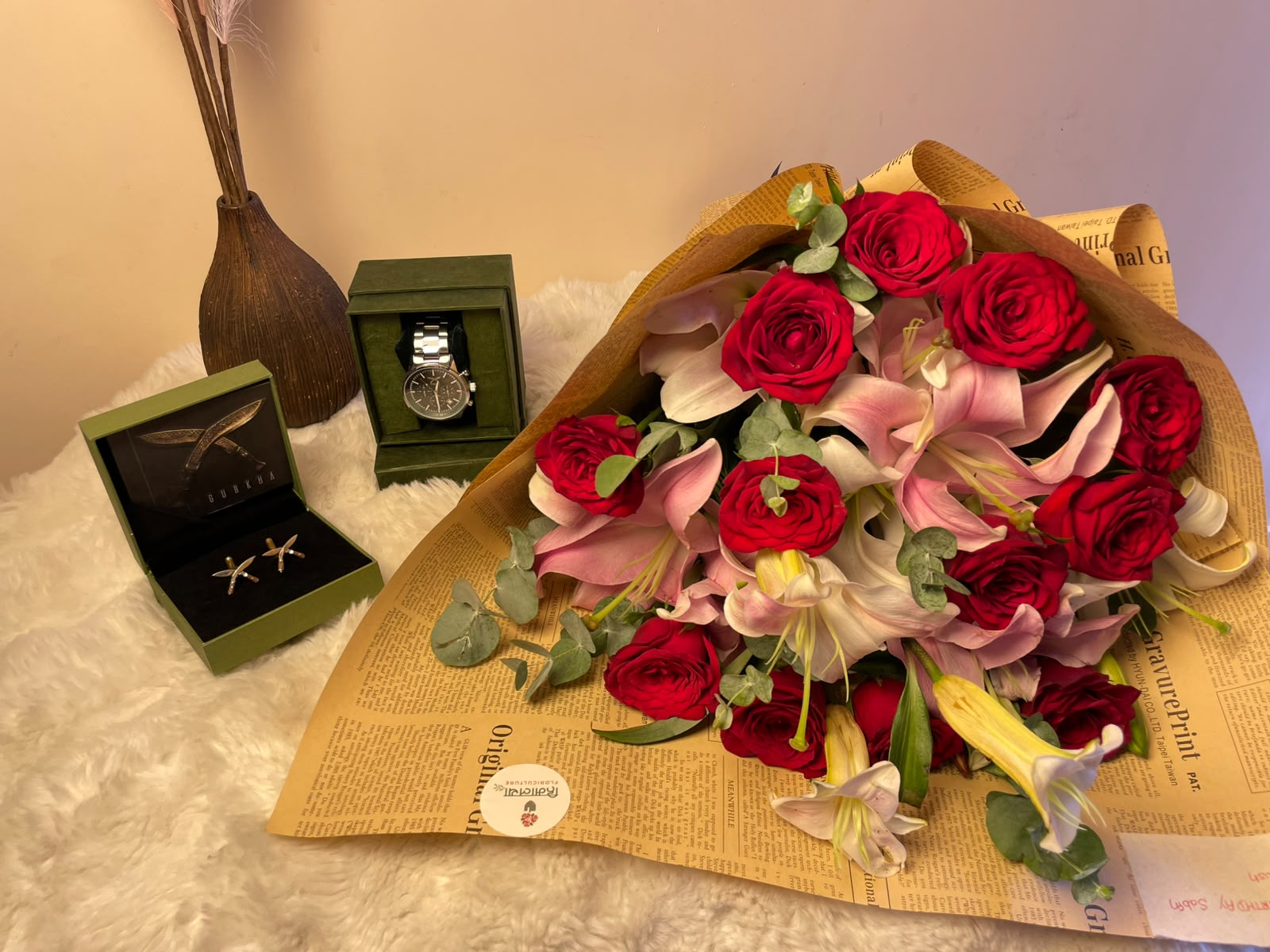 A premium and thoughtful gift set combining 1 men's watch, 1 pair of Khukuri brooches, and a beautiful mixed flower bouquet. The bouquet features 4 stems of pink lilies and 12 stems of red roses, complemented with Dollar Plant foliage and finished with an elegant vintage newspaper-style wrapper.