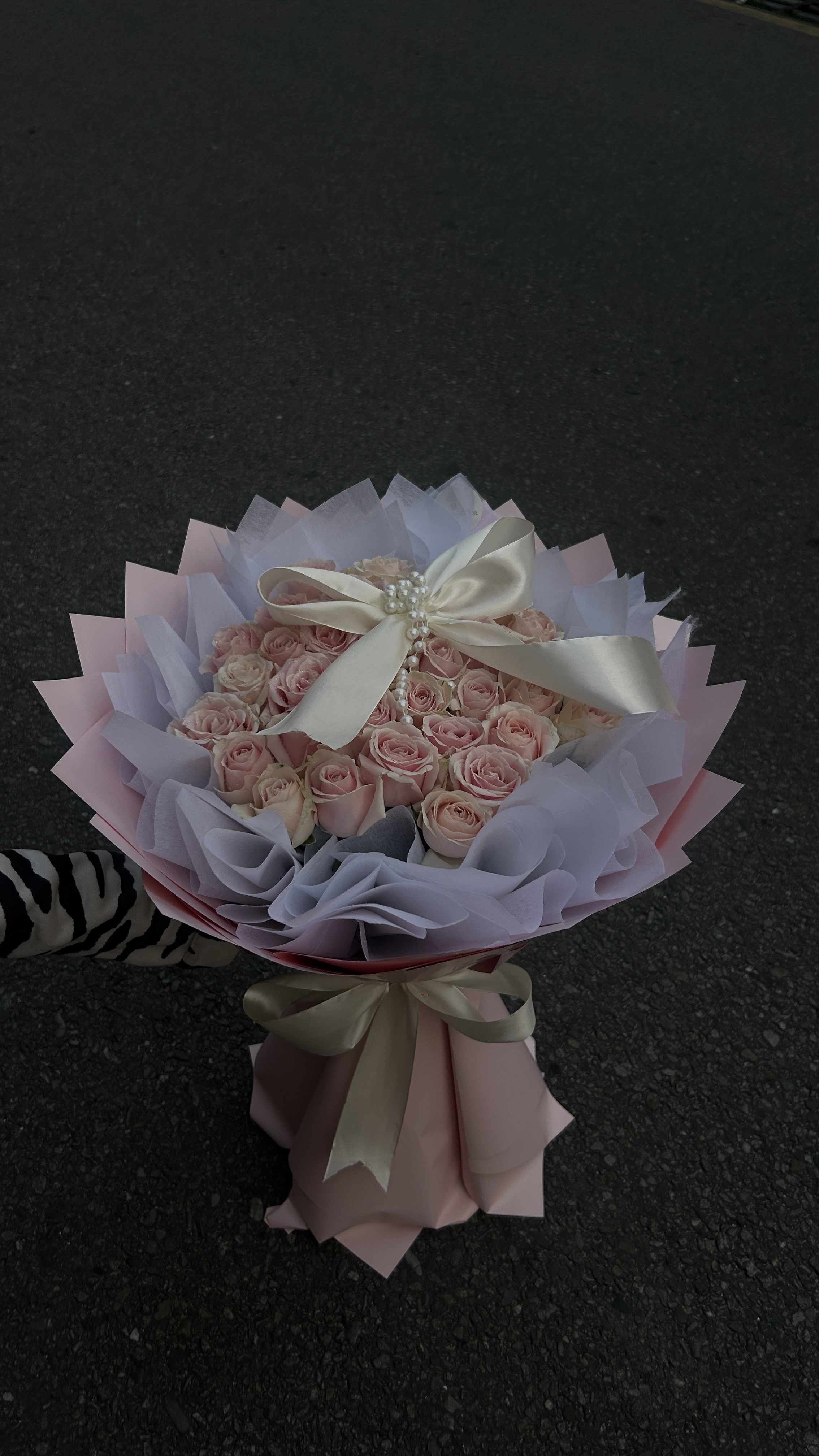 Pearl Ribbon Rose Bouquet An elegant bouquet featuring 30 pastel pink roses arranged in a bulky design with an oasis base. Finished with white and pastel pink wrapping, pearl details, and a white ribbon for a soft, luxurious look.