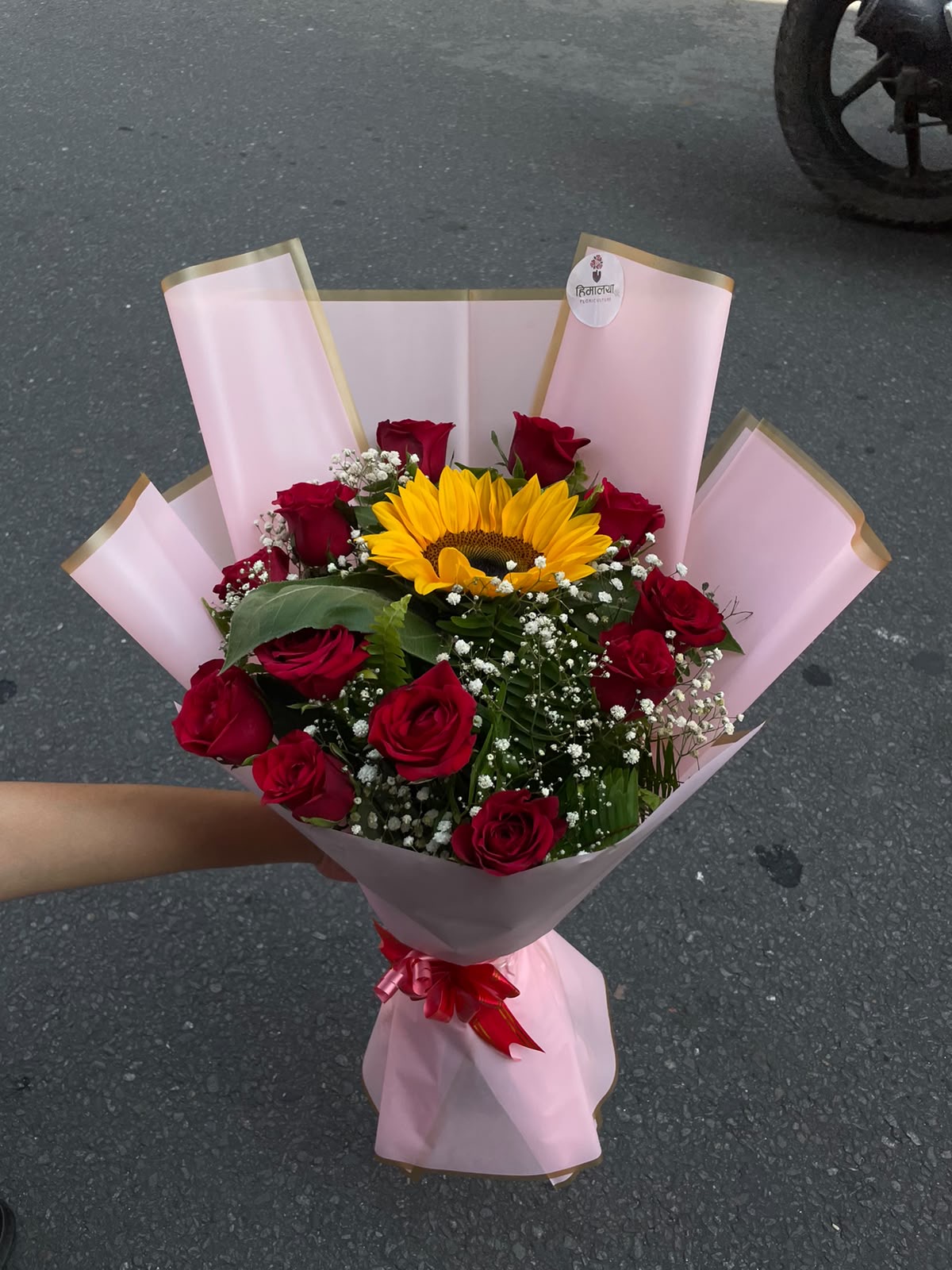 Sunshine Love Bouquet A vibrant combination of 12 red roses and a bright sunflower, finished with delicate gypsophila and a soft baby-pink wrap.