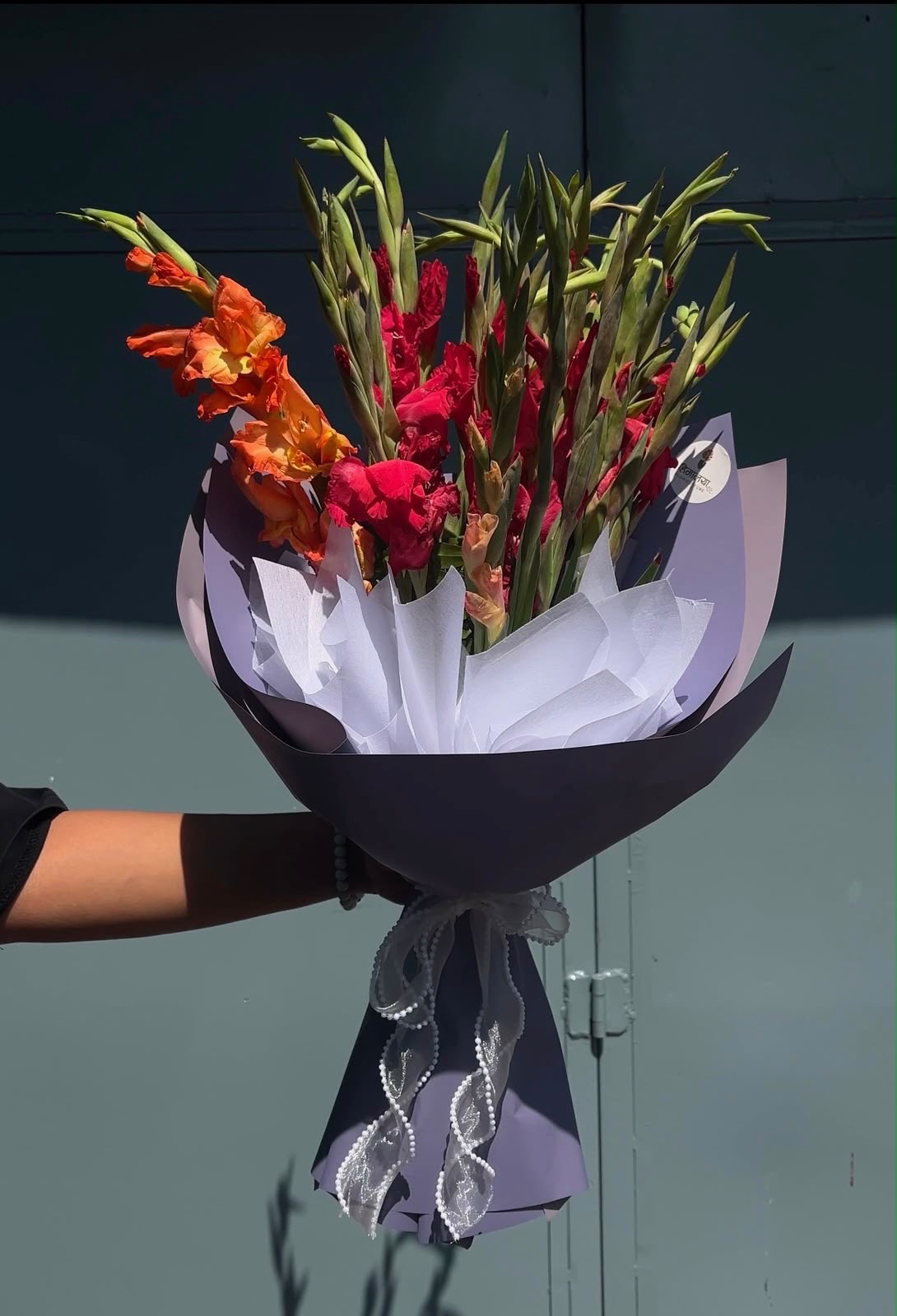 An elegant bouquet featuring 20 stems of gladiolus, beautifully wrapped in white and purple paper for a graceful and sophisticated appearance.