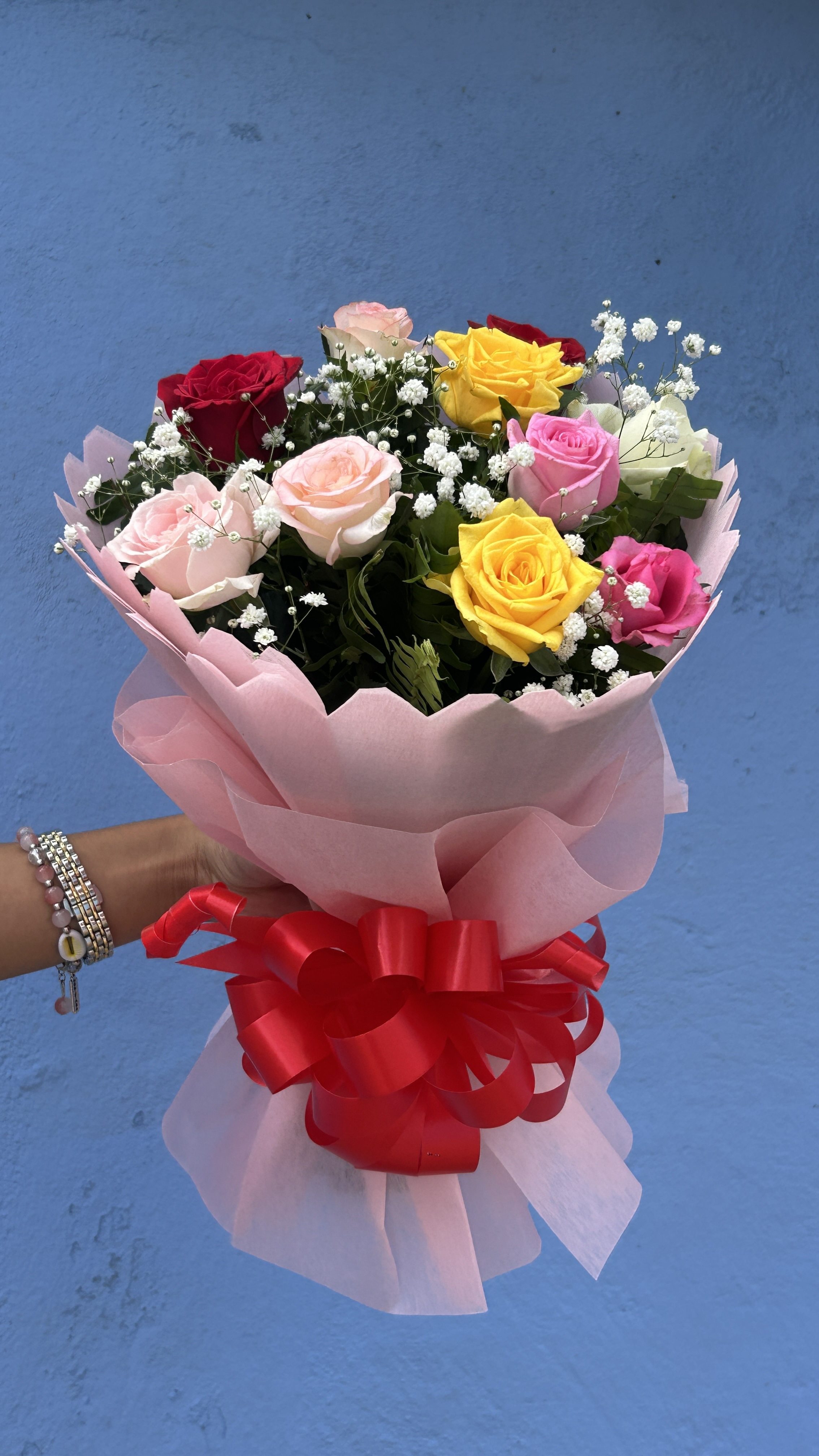 A vibrant bouquet of 10 fresh roses in red, blush pink, hot pink, yellow, and white, accented with baby's breath and greenery, wrapped in pink paper with a red satin ribbon. A perfect gift for anniversaries, birthdays, or any occasion to express love and appreciation.