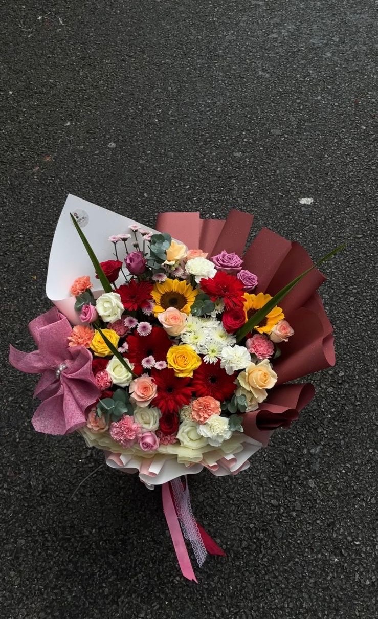 Sunshine Floral Bouquet A luxurious mixed bouquet featuring 2 Sunflowers and 45 stems of assorted fresh flowers, complemented with green leaves, decorative notes, and a beautiful bow, all finished in White and Brown Premium Wrapping.