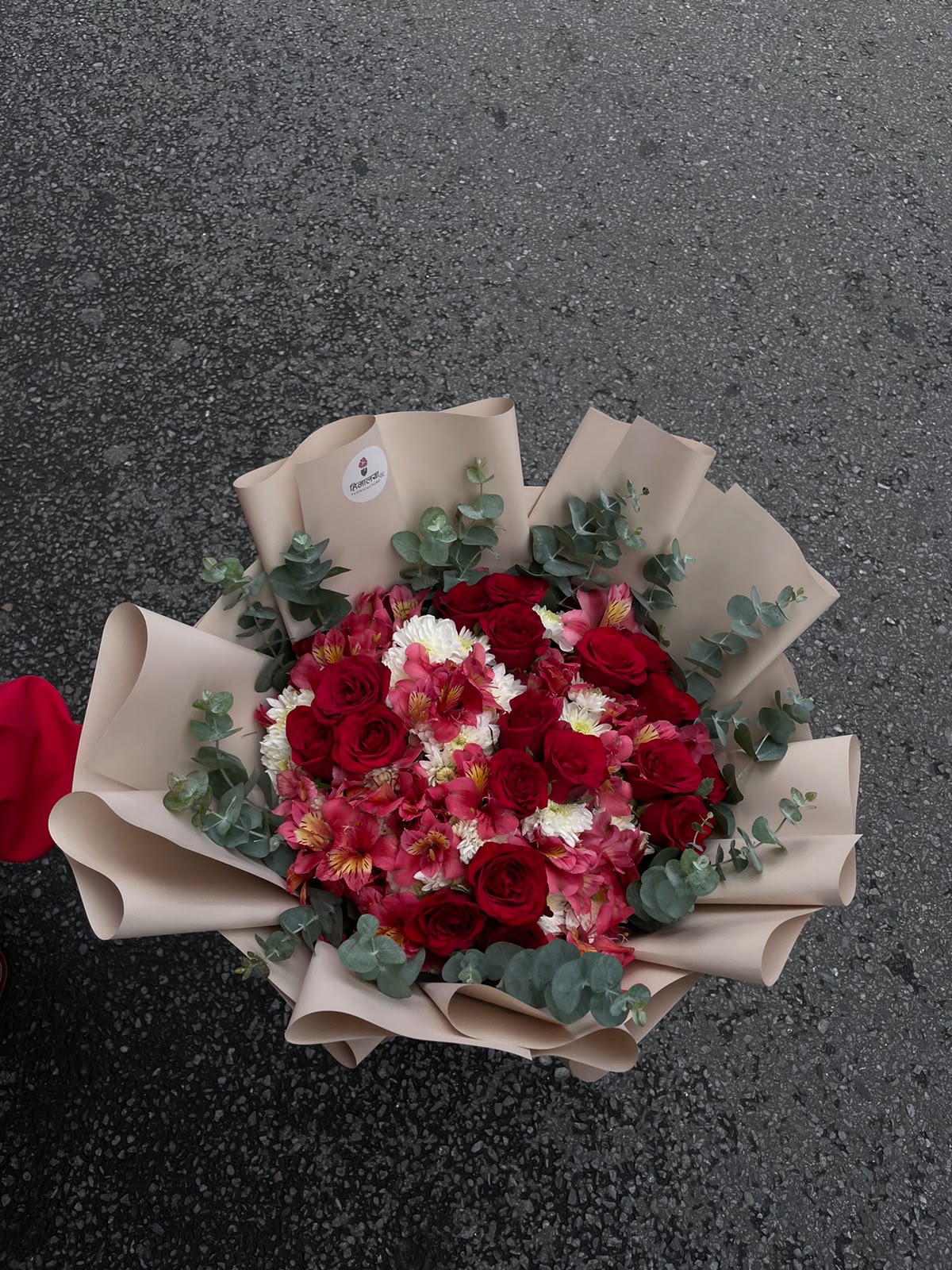 A beautiful bulky floral arrangement featuring 18 fresh red roses, 10 stems of white Godawari/Daisy, and Stomaria, carefully arranged on an Oasis base for a fuller and more structured look. The bouquet is finished with an elegant light brown wrapper, creating a warm and sophisticated presentation.