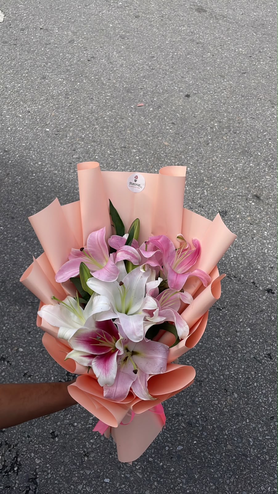 A graceful floral arrangement featuring 3 stems of pink and white lilies, beautifully arranged and finished with an elegant cream wrapper. The soft combination of pink, white, and cream creates a sophisticated and delicate presentation.