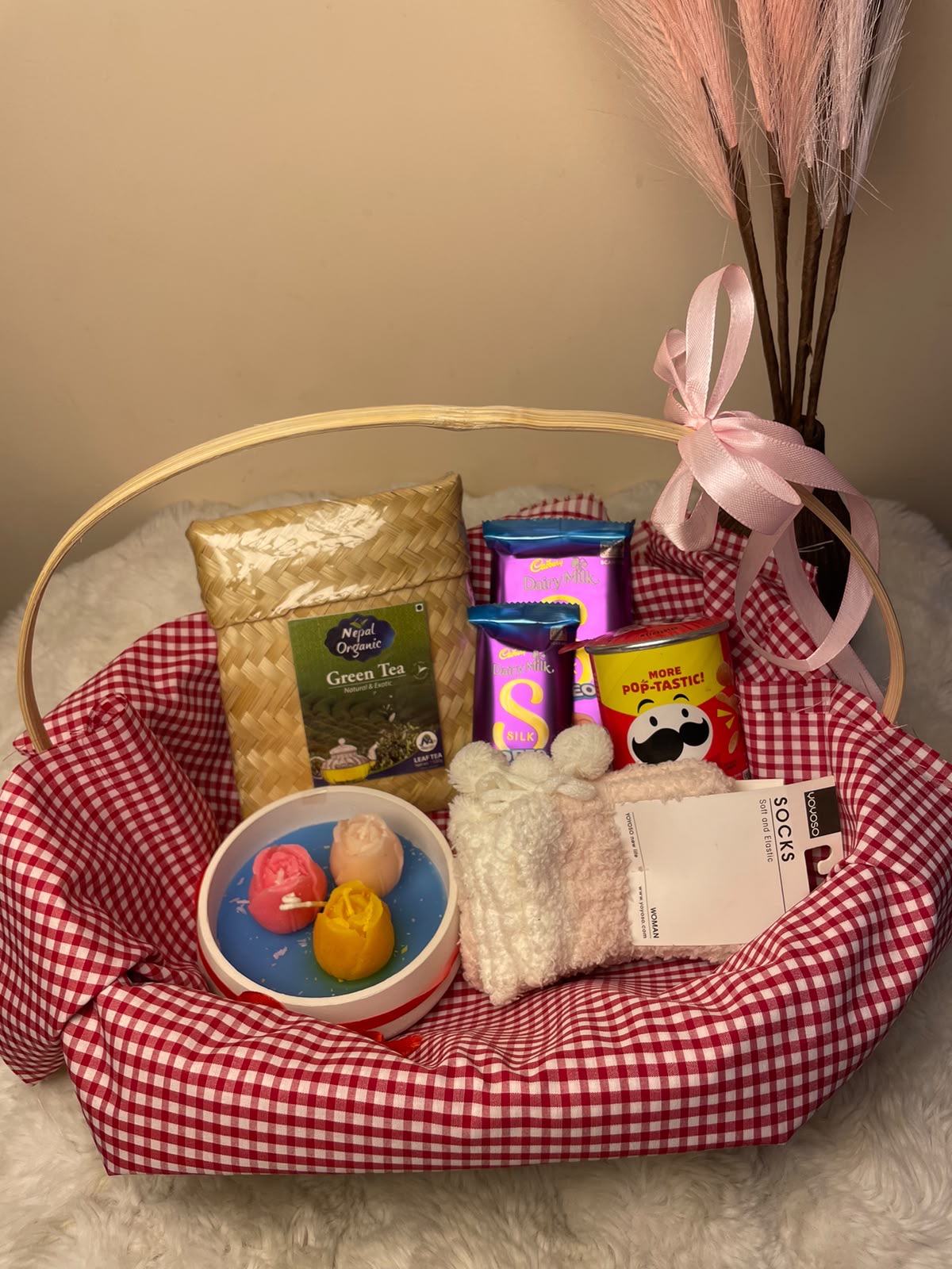 A warm and thoughtful festive gift set featuring a scented candle, comfortable socks, chocolates, mini Pringles, and green tea.