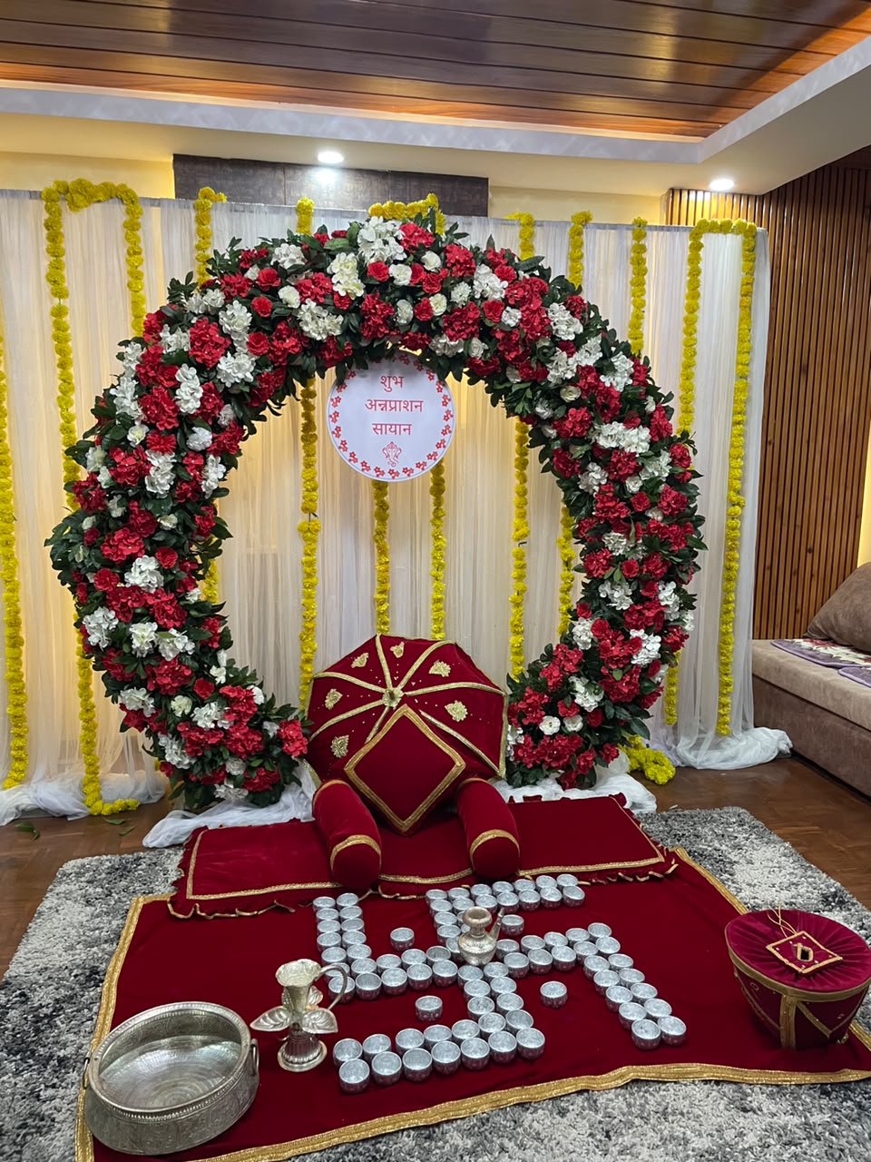 A custom central badge placed directly in the floral arch featuring the child's name (e.g., "Shubh Annaprasan Sayan" in Devanagari script).