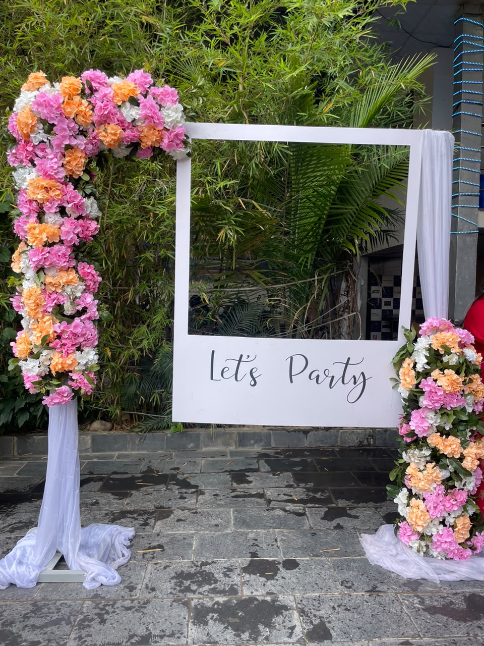 This decor perfectly blends modern elegance with a romantic, natural aesthetic. The stark white geometric frame creates a crisp contrast against outdoor landscapes, while the soft, colorful floral clusters add warmth and festive charm. Beyond being a stunning visual focal point for your venue, the integrated seating transforms the setup into an engaging experience, encouraging guests to sit, relax, and create lasting memories together in front of the camera.