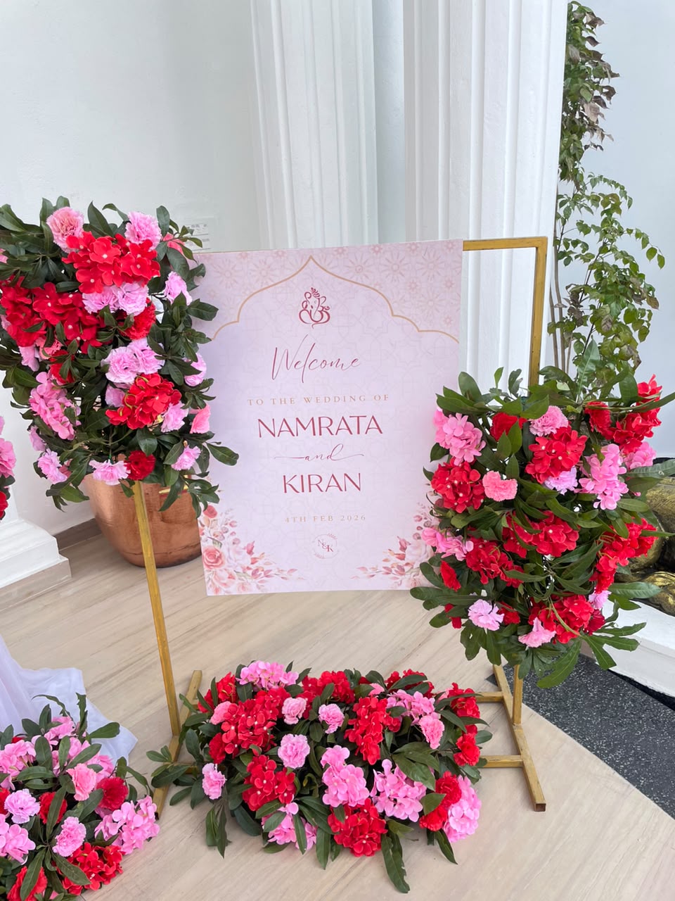 This welcome setup creates an immediate atmosphere of elegance and celebration the moment guests arrive. The vivid pink floral accents offer a captivating pop of color that stands out beautifully in entranceways and foyer spaces, providing both a functional greeting sign and an eye-catching photo backdrop that sets a romantic, sophisticated tone for the entire event.